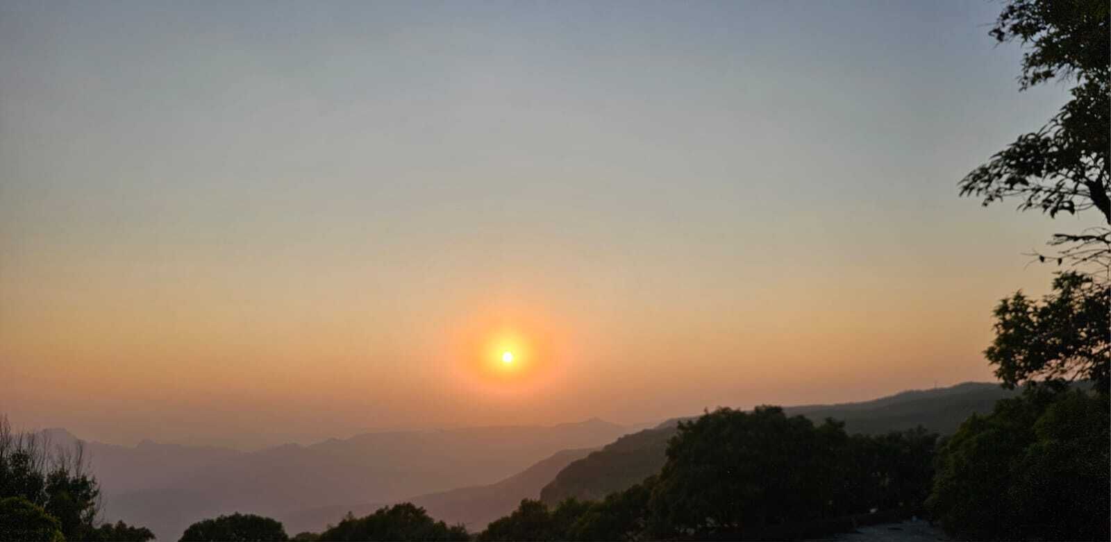 Ein Sonnenuntergang über einer Berglandschaft, im Vordergrund Bäume.