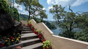 A set of stone steps leading up to a terrace with potted plants and a view of a lake. - Hotel Himalaya (Nainital)