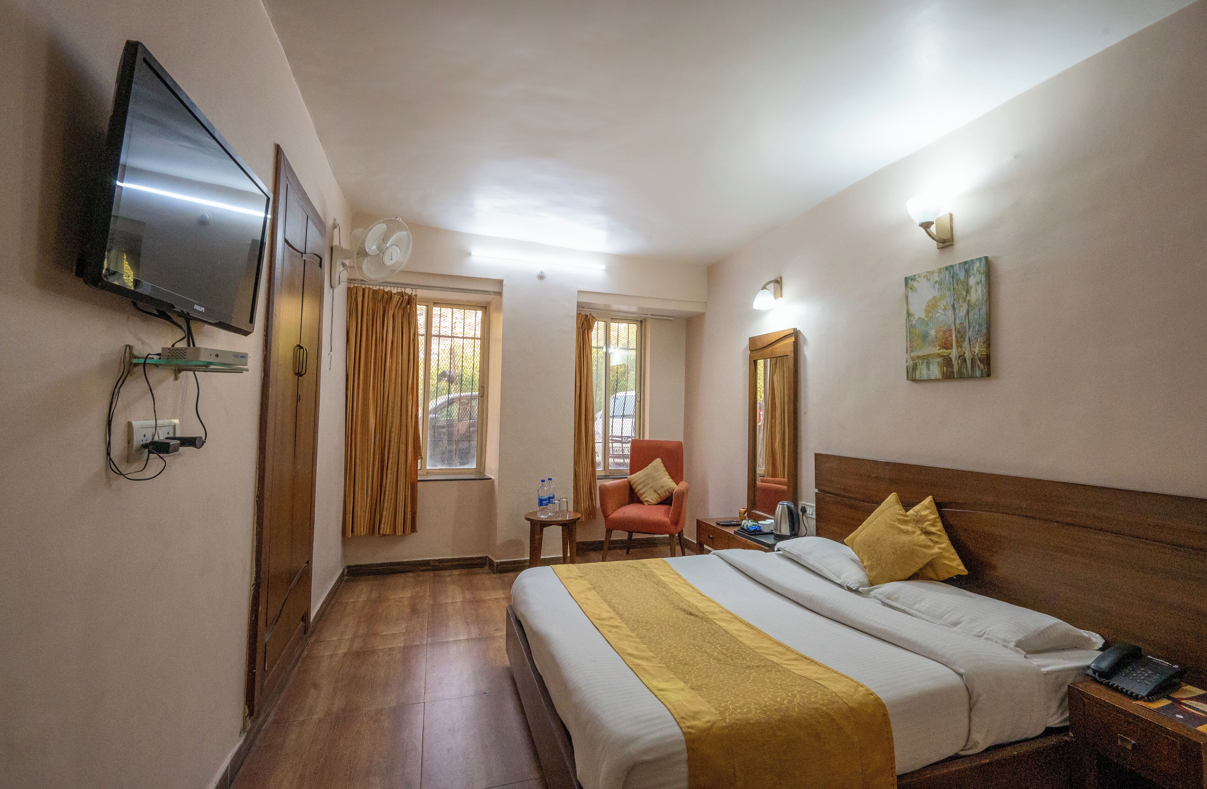 A hotel room with a bed, a TV mounted on the wall, a chair, a small table, and a window with curtains.