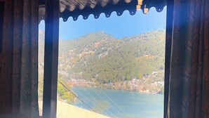 A room with a wooden ceiling, a table, a sofa, and a window with curtains. - Hotel Himalaya (Nainital)