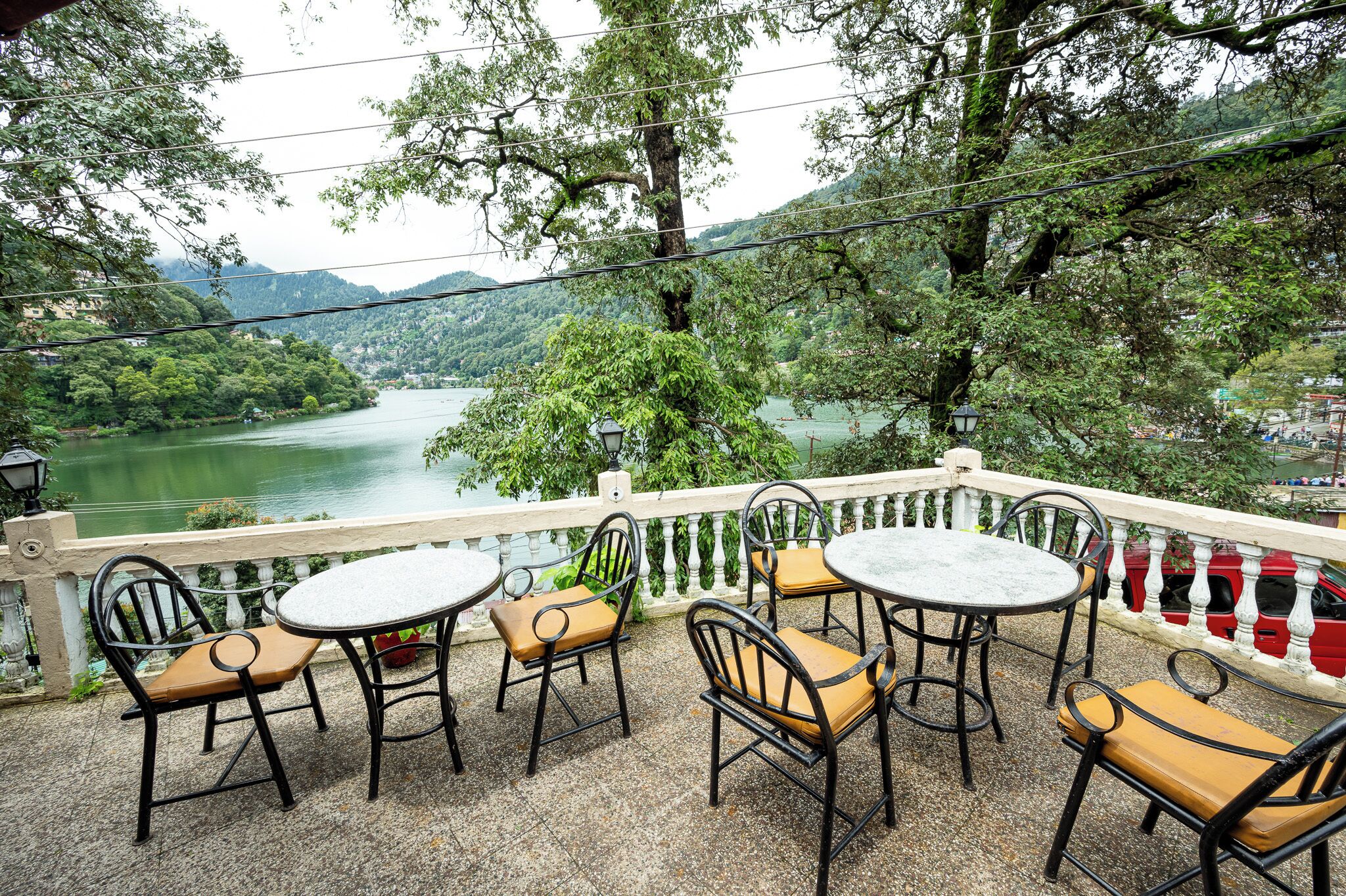 A terrace with round tables and chairs, overlooking a river and hills.