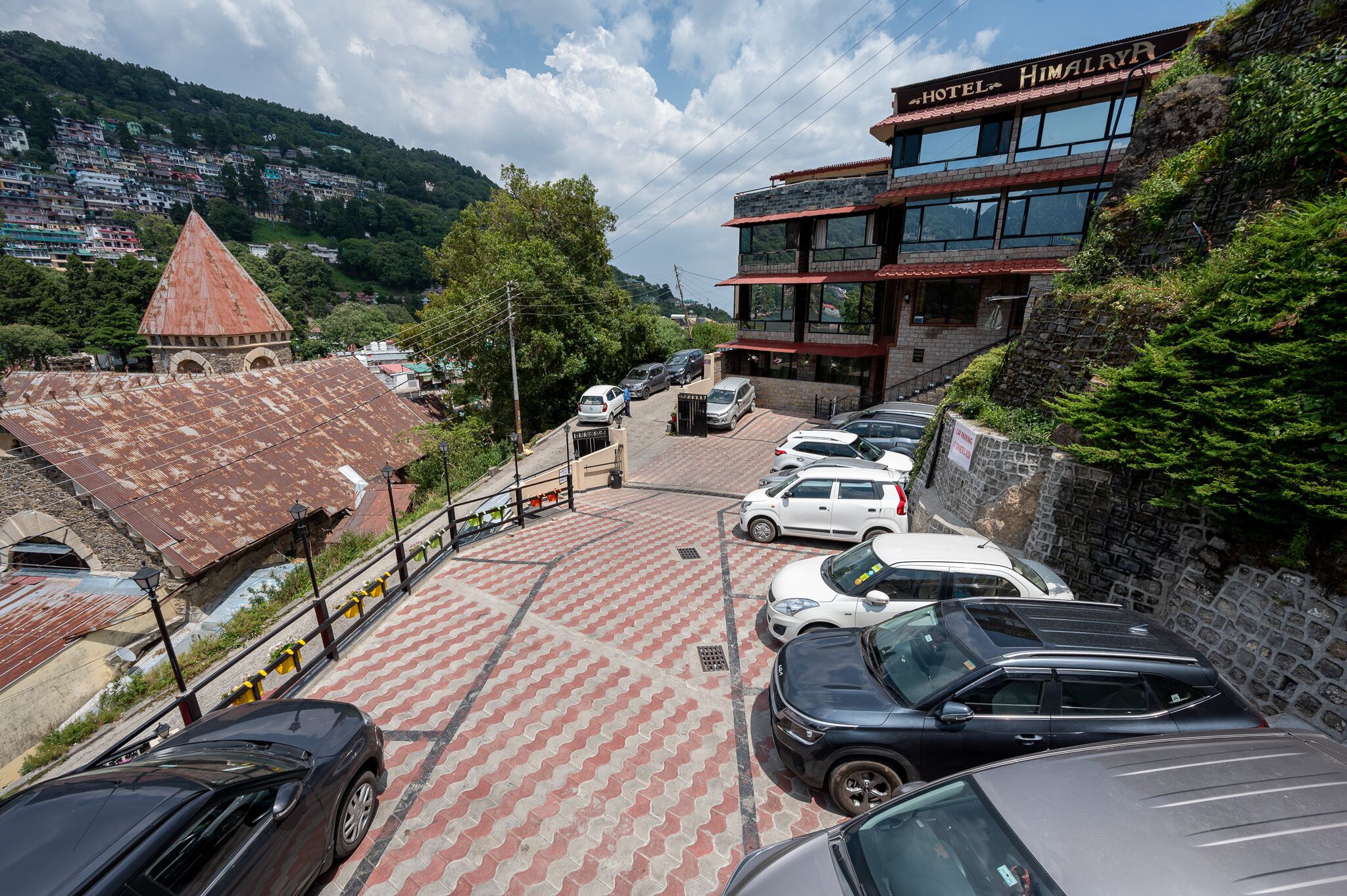 Ett hotell som heter ”Himalaya”, med en parkeringsplats, en byggnad med rött tak och en bergig bakgrund.