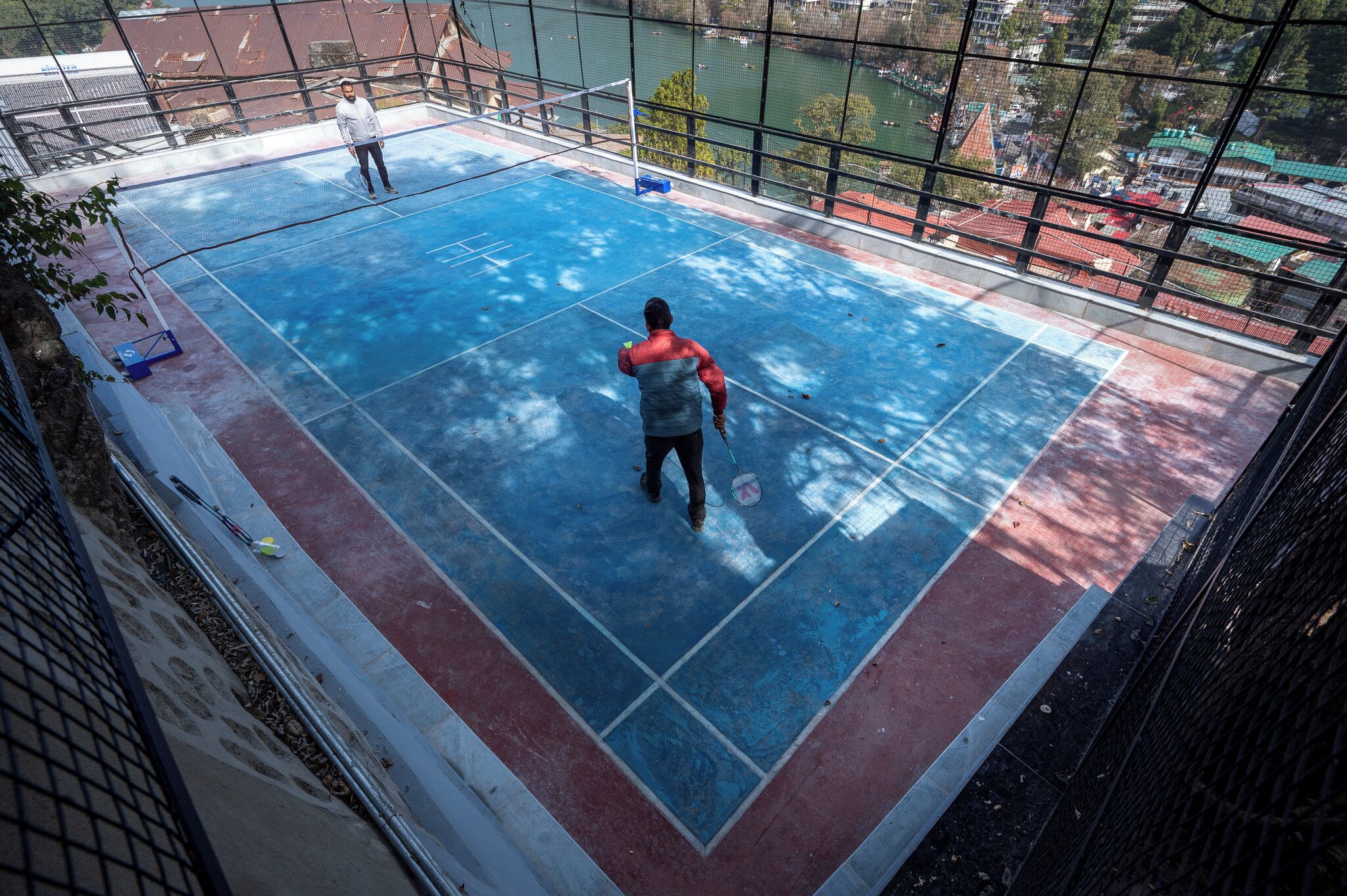 A view of a rooftop tennis court with a net, surrounded by a metal fence.