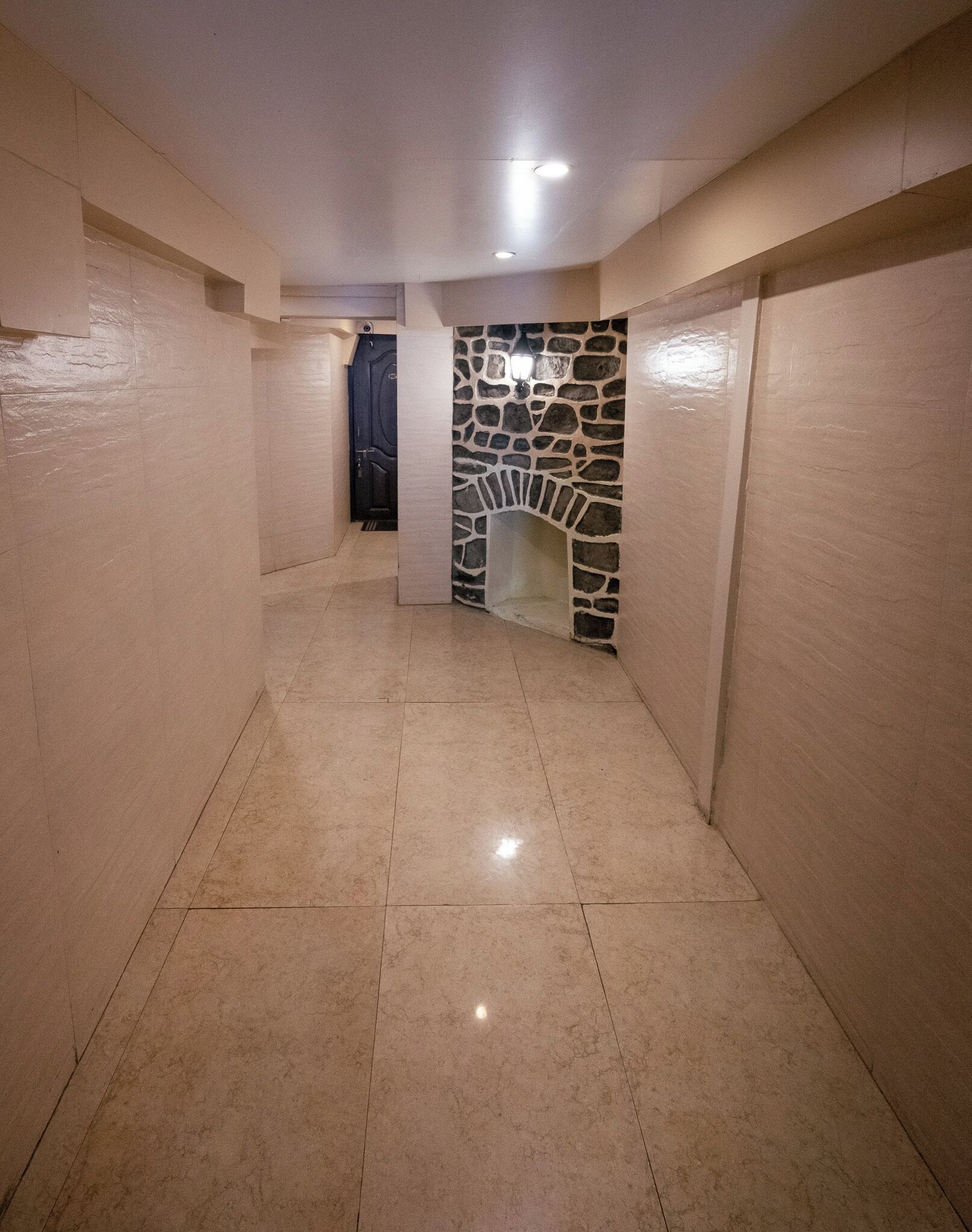 A hallway with tiled floors and walls, leading to a stone fireplace with a modern design.