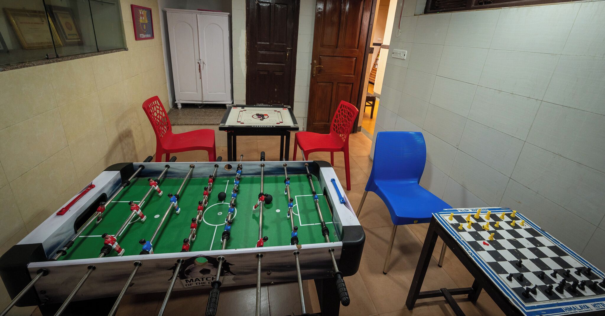 A foosball table in a room with a chessboard, red and blue chairs, and a small table.
