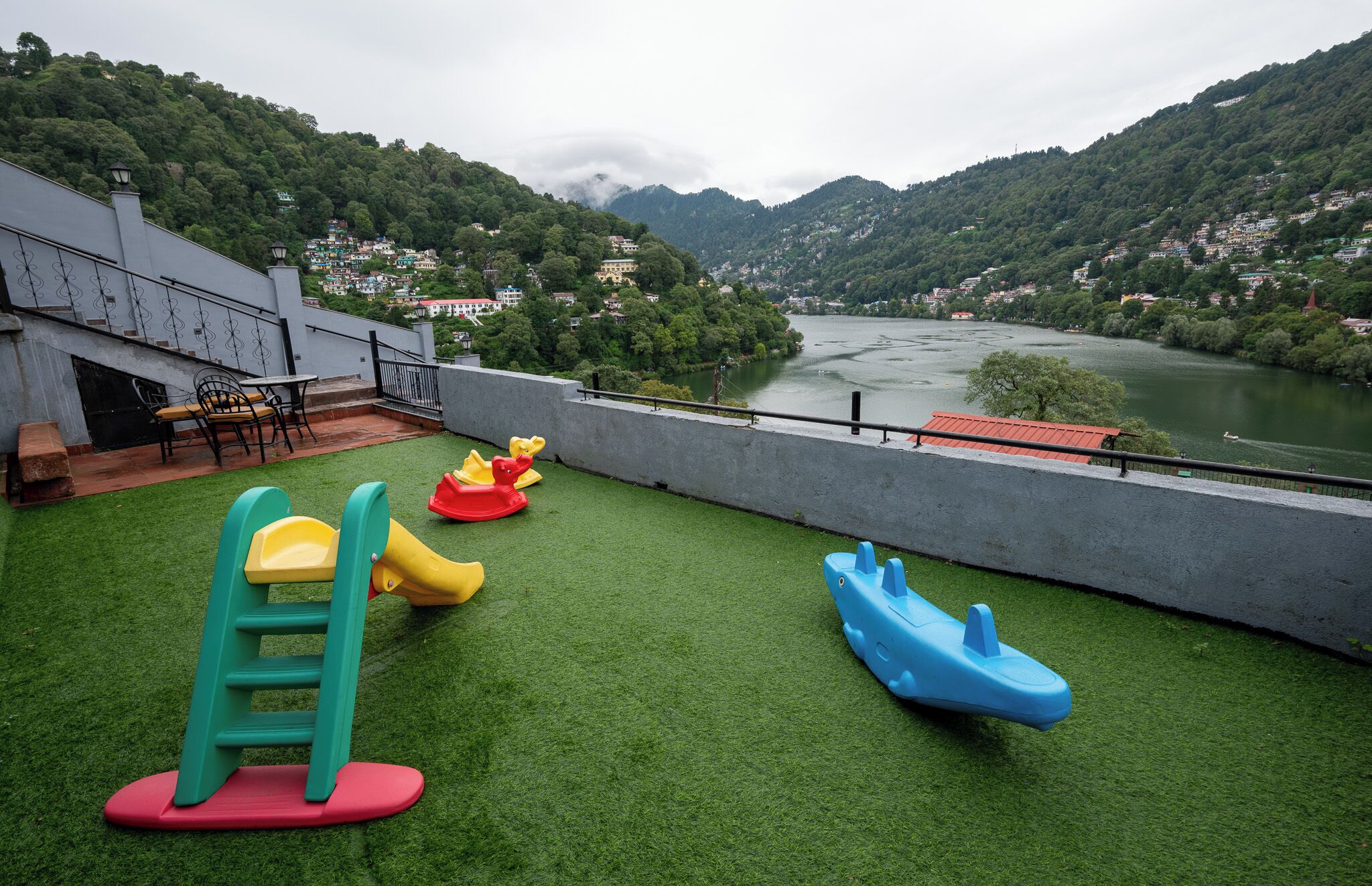 A rooftop playground with a slide, a climbing ladder, and two rocking horses, overlooking a river and hills.