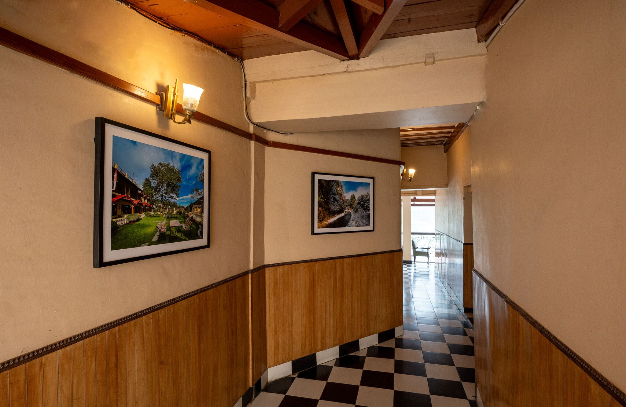 A hallway with wooden paneling, black and white checkered flooring, and framed landscape photographs on the walls.