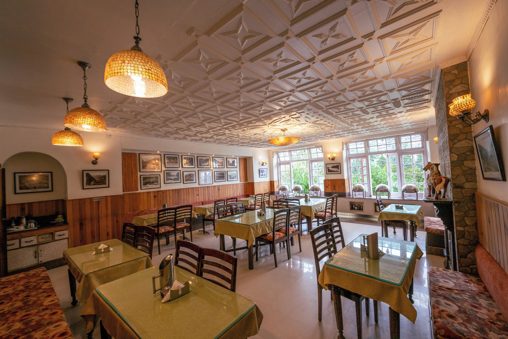 A dining area with multiple tables and chairs, wooden paneling on the walls, and hanging pendant lights.