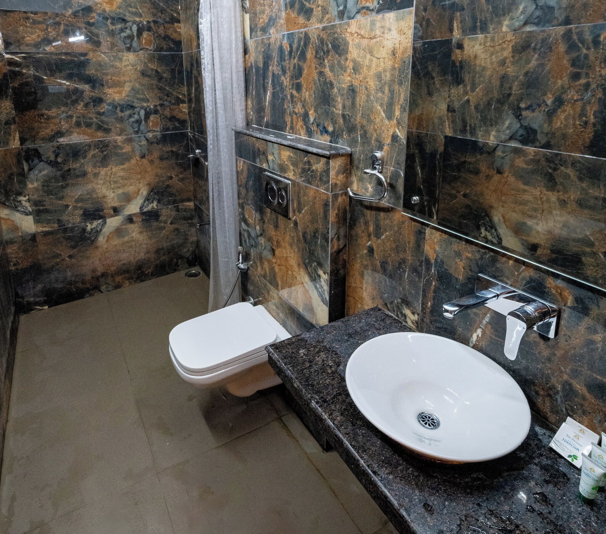 Une salle de bain avec un mur en marbre, des toilettes blanches et un lavabo avec un drain.