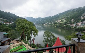 A view of a river valley with a castle-like structure in the foreground, surrounded by lush greenery and a mountainous backdrop. - Hotel Himalaya (Nainital)