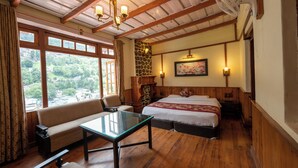 A room with a wooden ceiling, a sofa, a bed, a table, and a view of greenery outside. - Hotel Himalaya (Nainital)