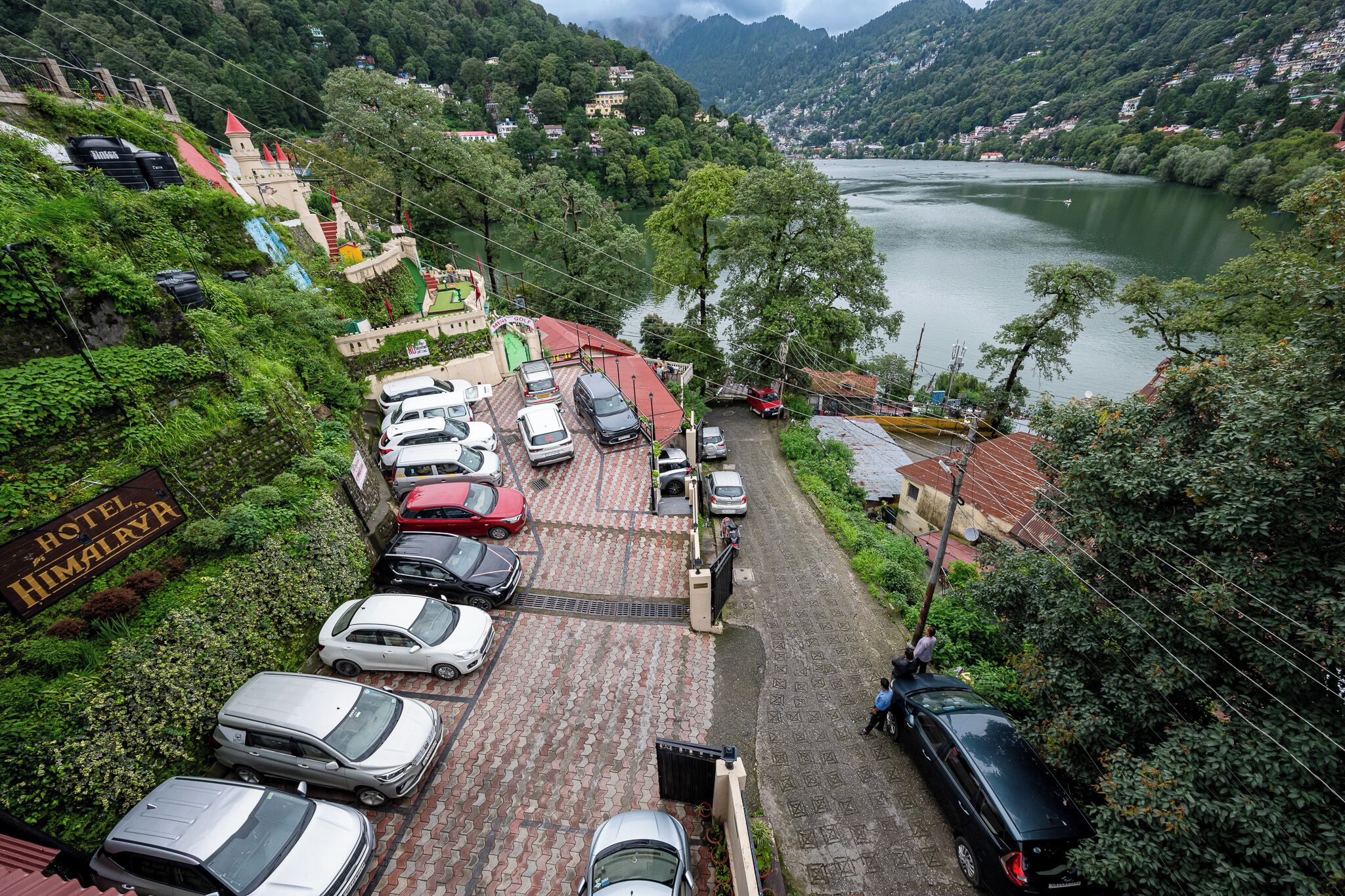 A hotel with a parking lot, a river in the background, and a mountainous landscape.