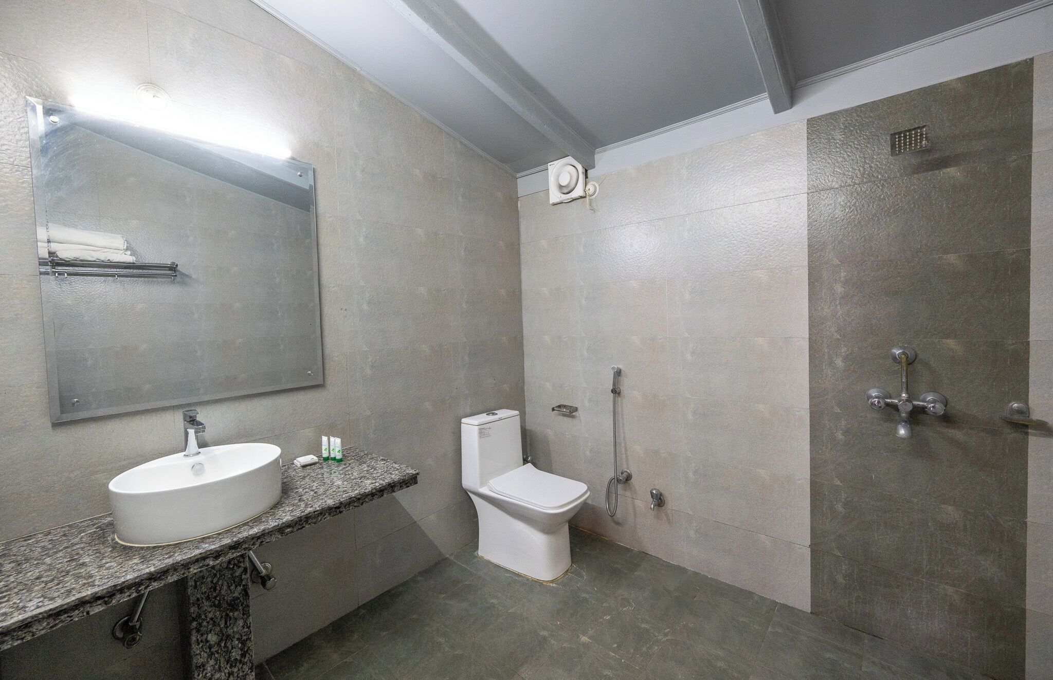Un baño moderno con encimera de granito, un lavabo blanco, inodoro y zona de ducha.