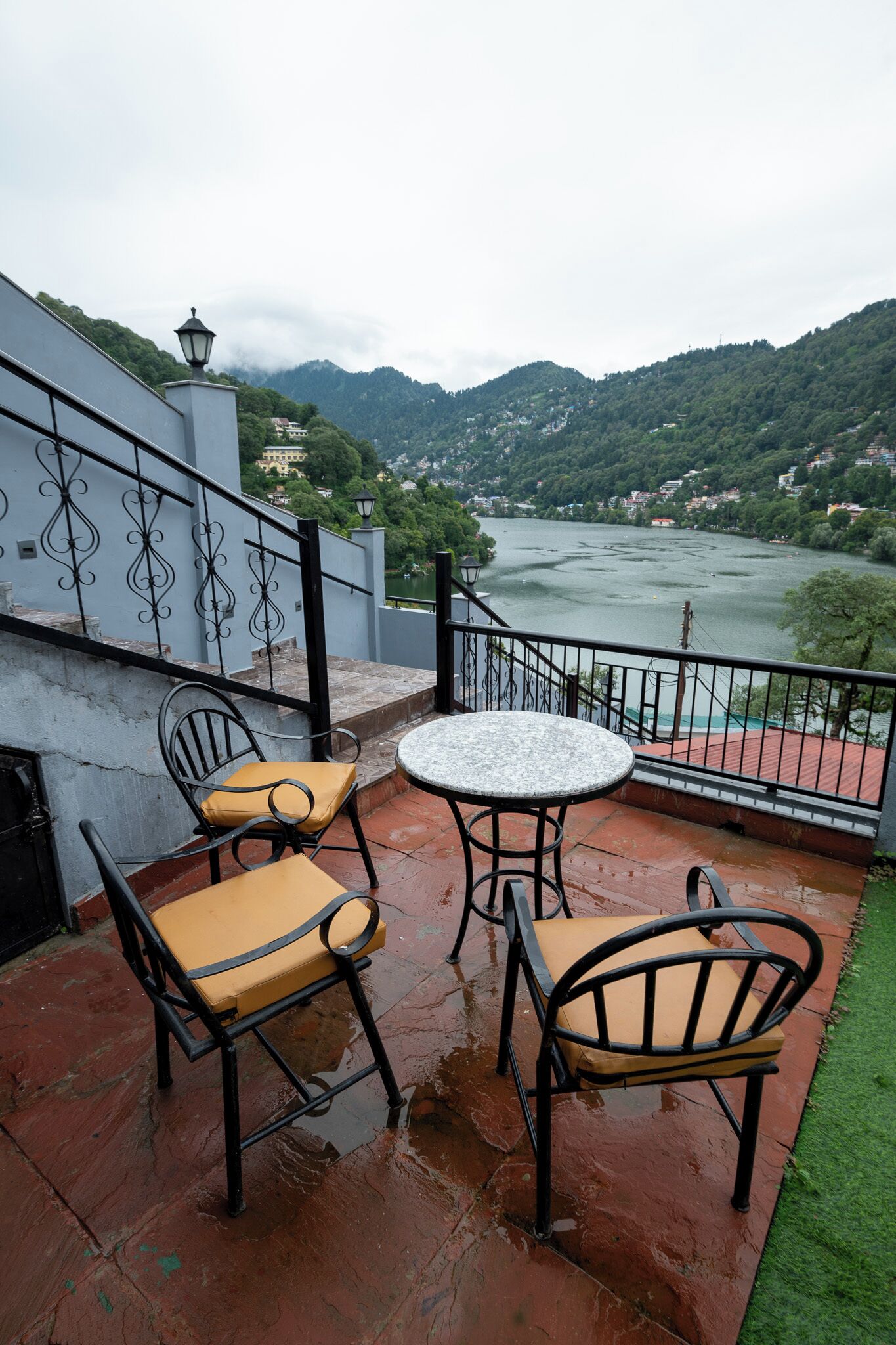 Un balcón con dos sillas y una mesa, con vistas a un río y colinas.