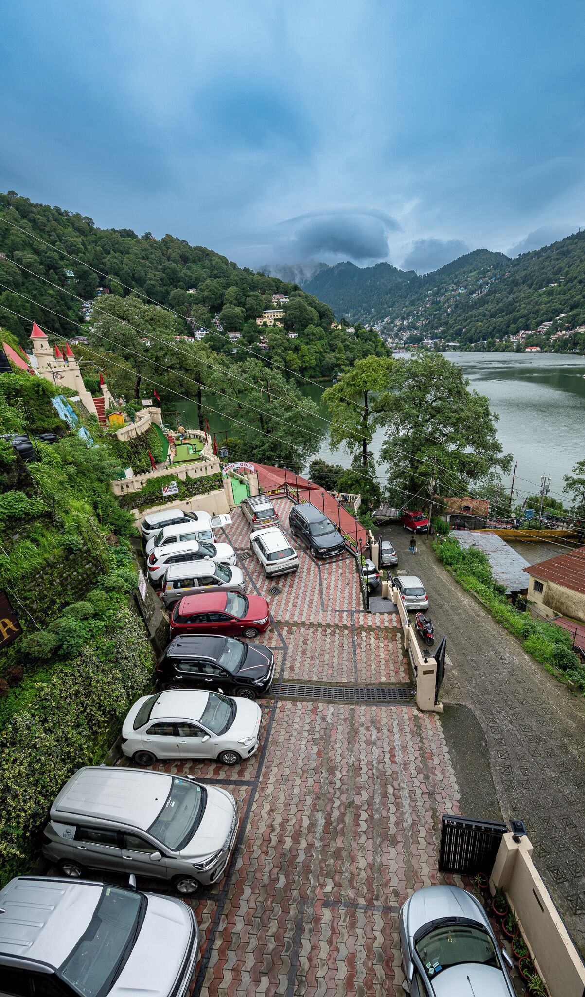 A parking area with cars, a building with a red roof, and a lake in the background.