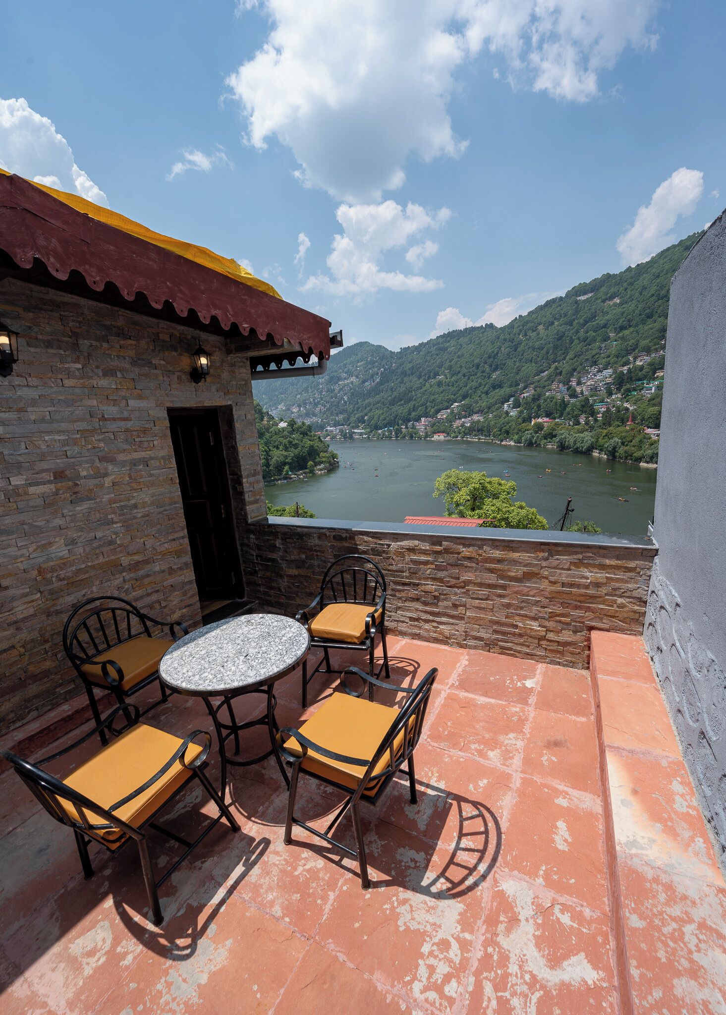 Une terrasse avec une table ronde et quatre chaises, un mur en pierre et une vue sur une rivière et des montagnes.