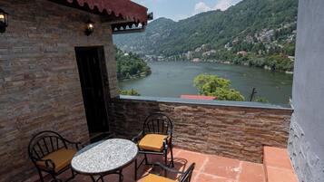 A terrace with a round table and four chairs, a stone wall, and a view of a river and mountains.