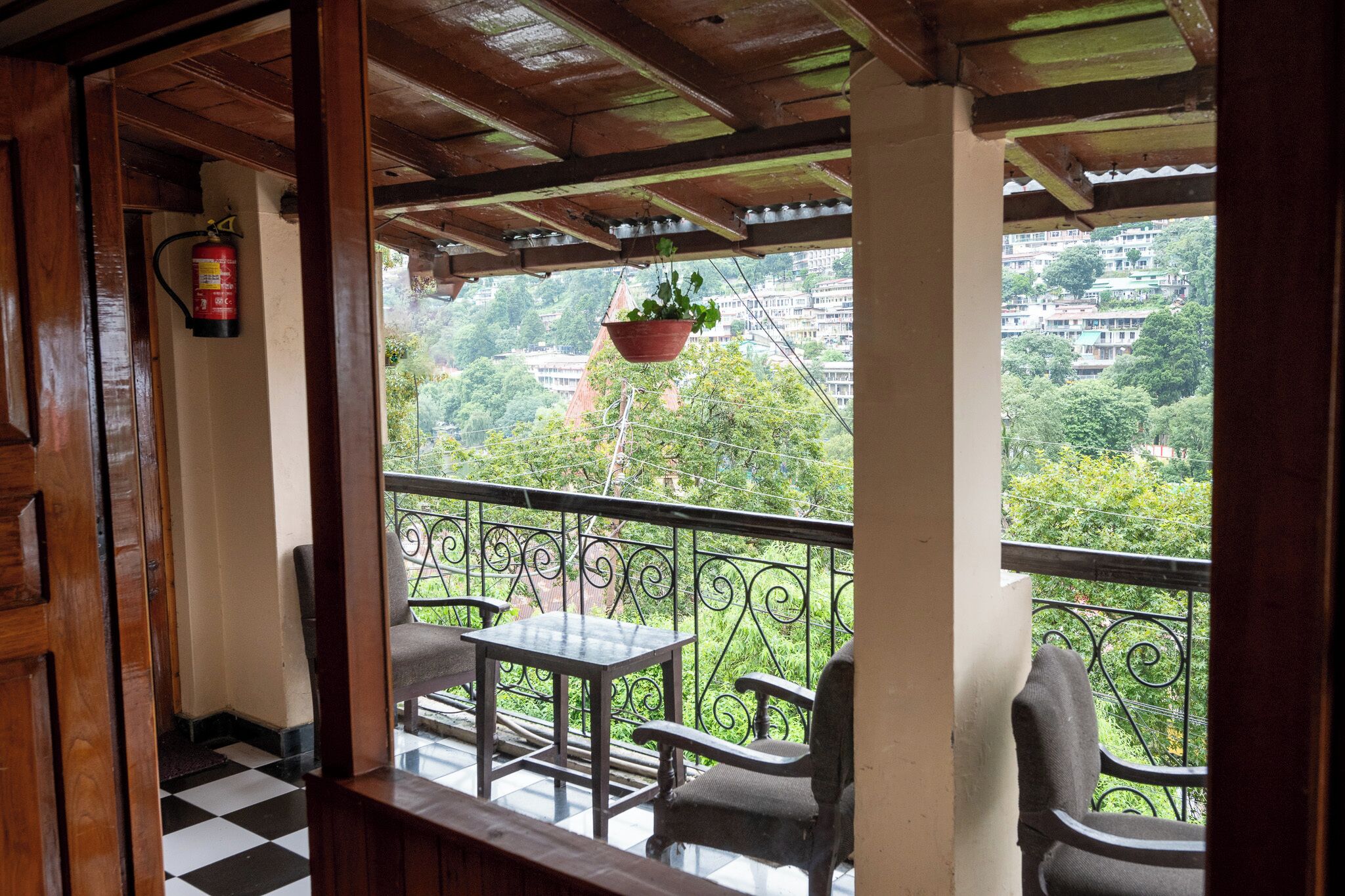 A balcony with a checkered floor, a table, and two chairs. A fire extinguisher is mounted on the wall.