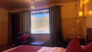 A room with a bed, a chair, a table, and a window with curtains. - Hotel Himalaya (Nainital)