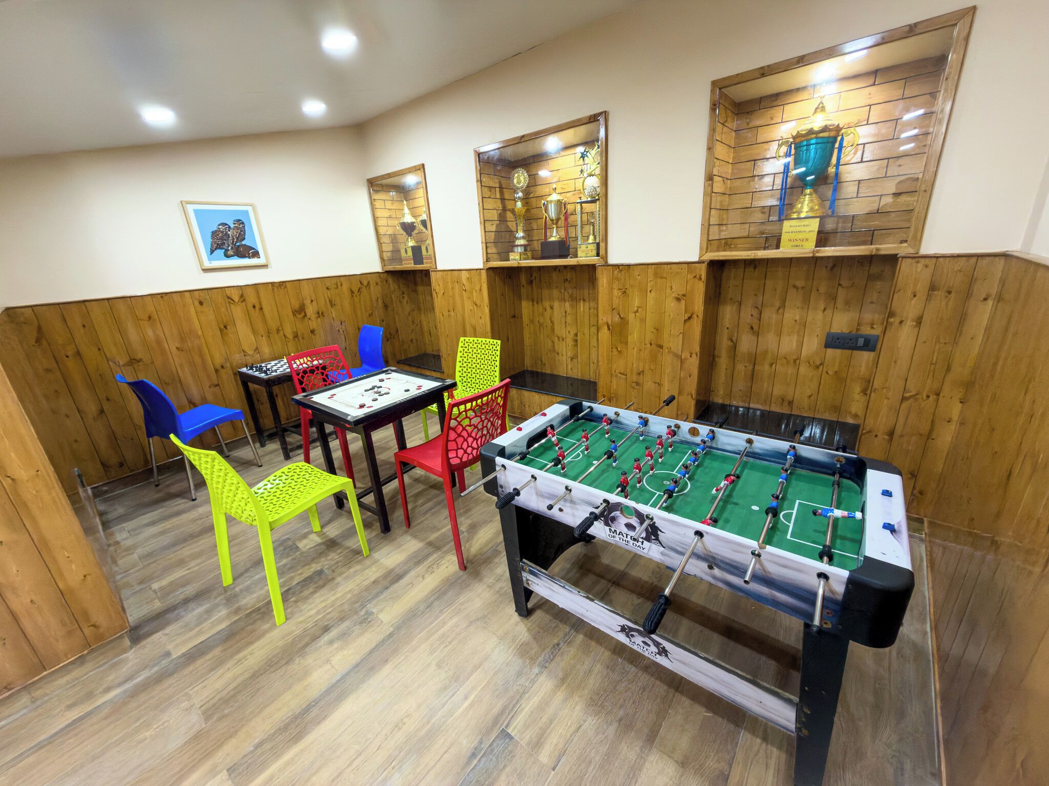 A room with a foosball table, colorful chairs, and trophies on shelves.