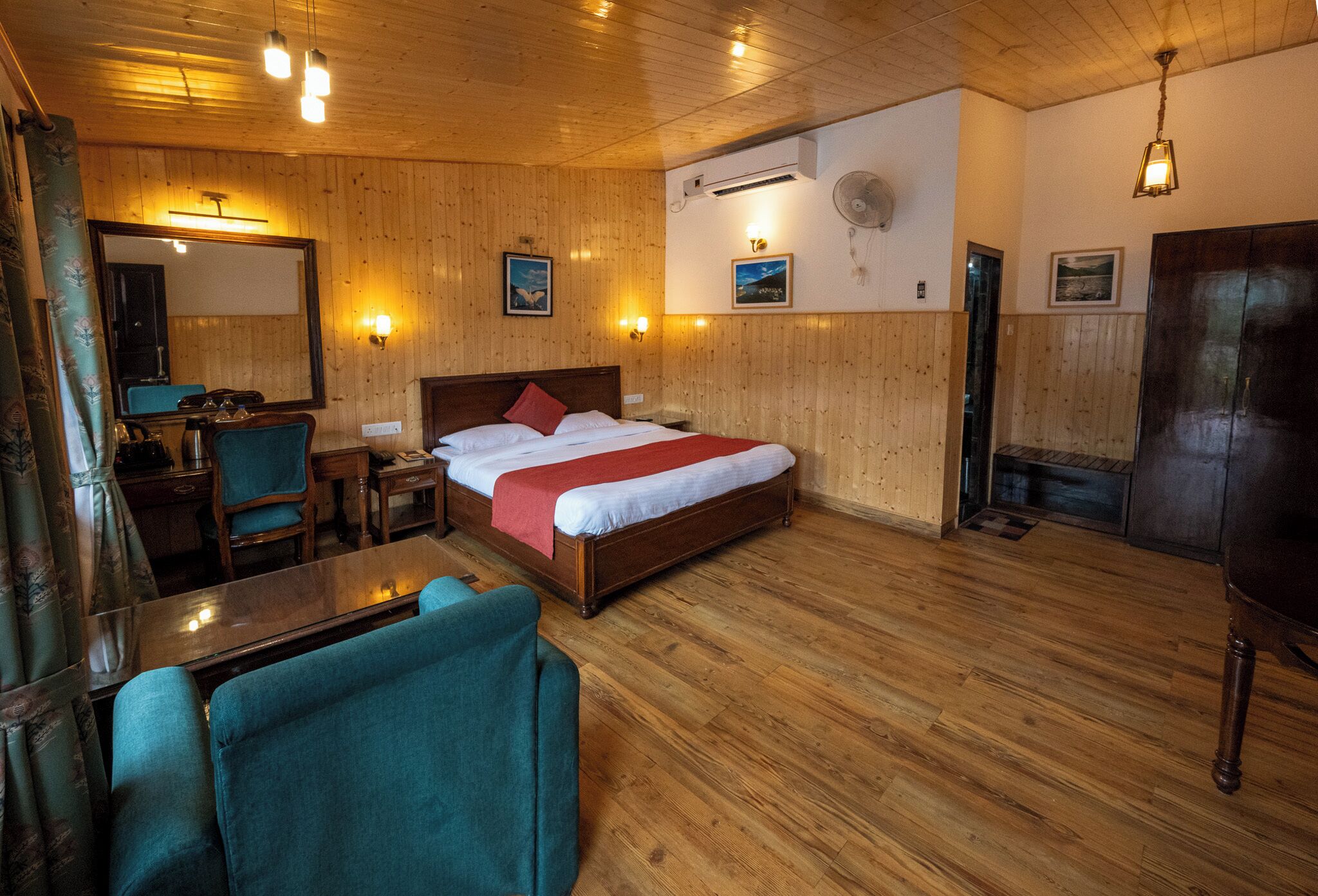A wooden-paneled room with a bed, a desk, chairs, and a fireplace.