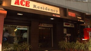 Exterior de ACE Residency, con un cartel, entrada y plantas en macetas.