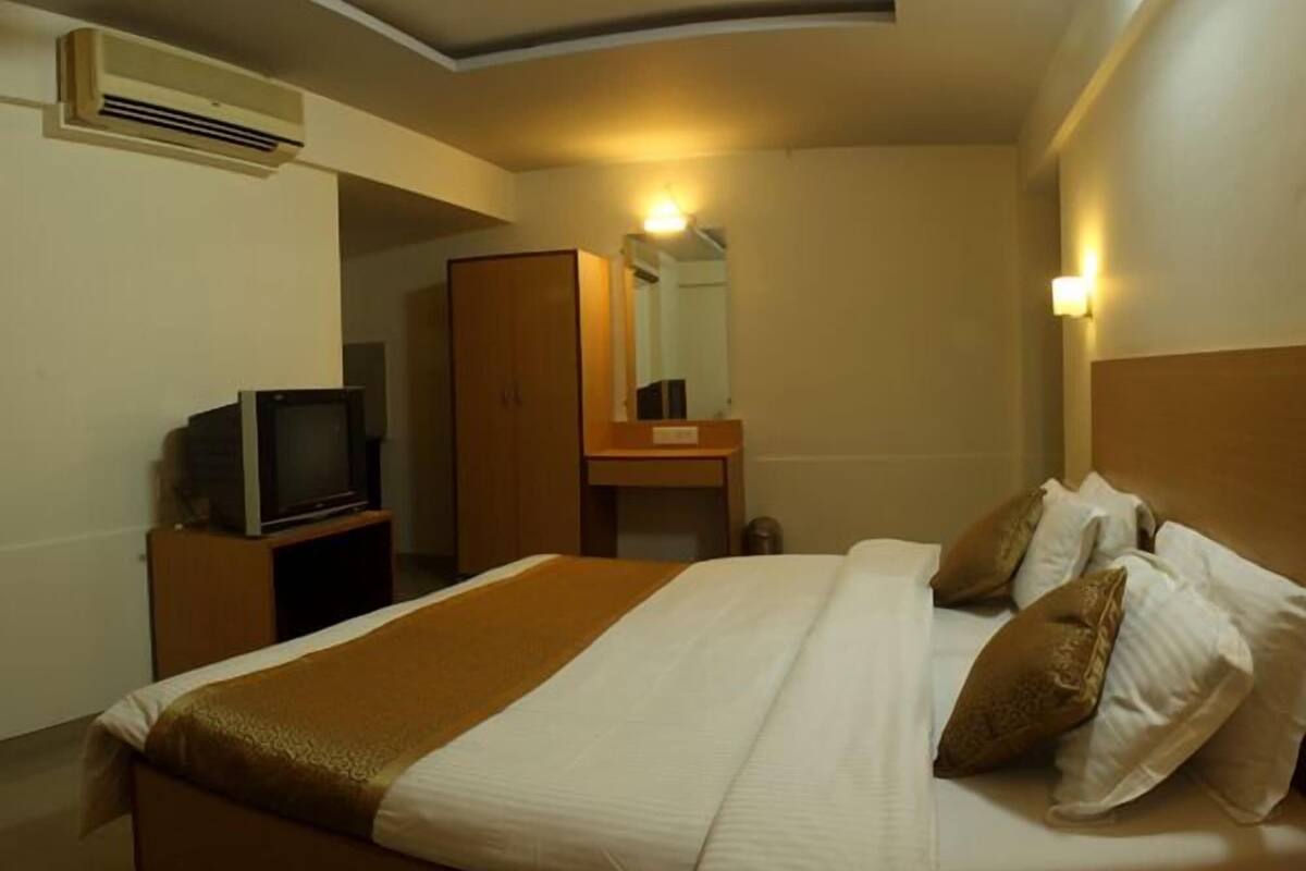 A hotel room with a bed, a television on a wooden stand, a wardrobe, a bedside table, and a mirror.