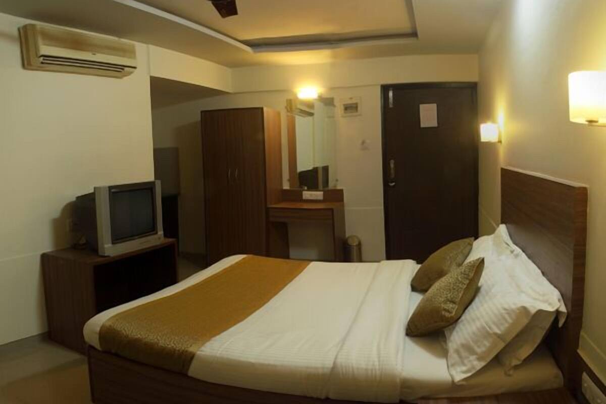 A hotel room with a bed, a television on a stand, a wardrobe, a mirror, and a door.