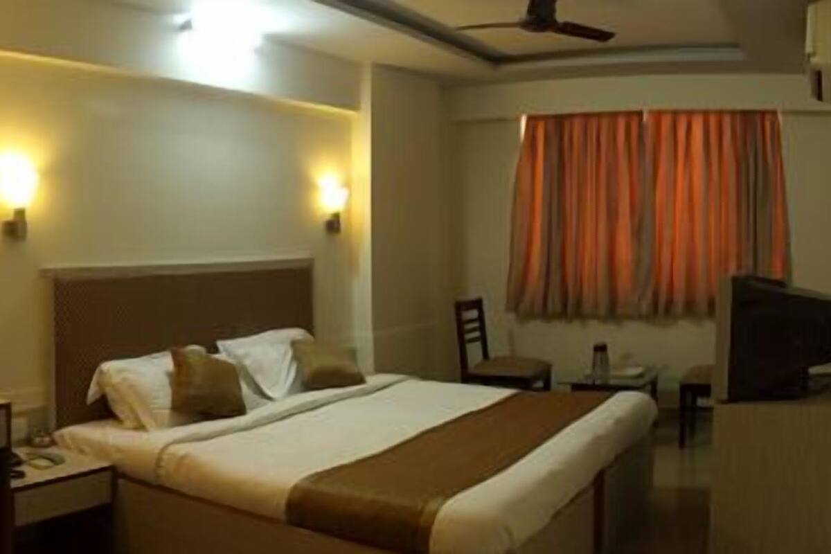 A hotel room with a bed, bedside table, lamp, and a television.
