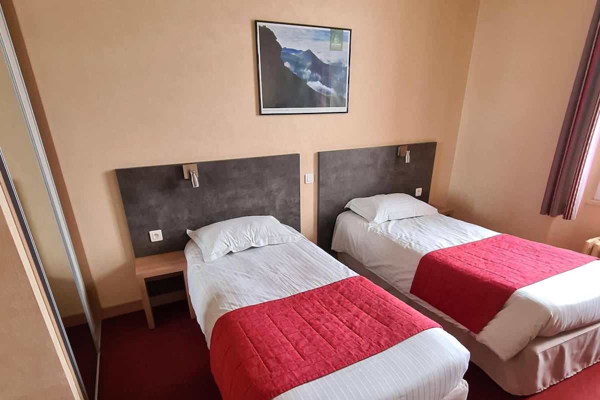A hotel room with two beds, a nightstand, a red carpet, and a framed picture on the wall.