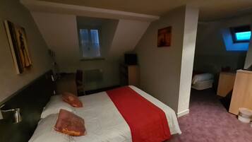 Een slaapkamer met een bed, een klein bureau, een stoel, een televisie en een raam.