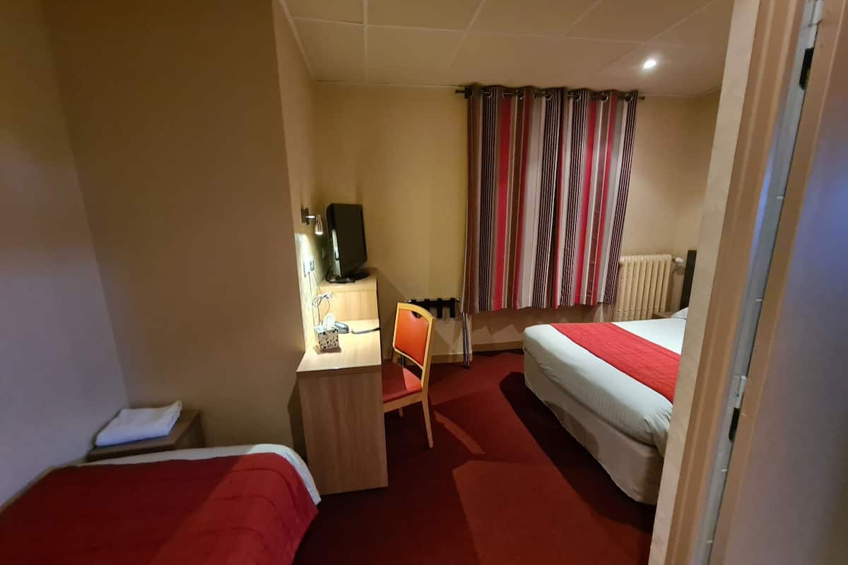 A hotel room with two beds, a desk with a computer, a chair, and a window with striped curtains.