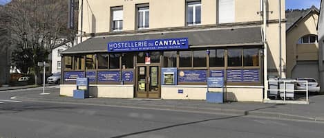 A building labeled "HOSTELLERIE du CANTAL" with a signboard and information displays at the entrance.