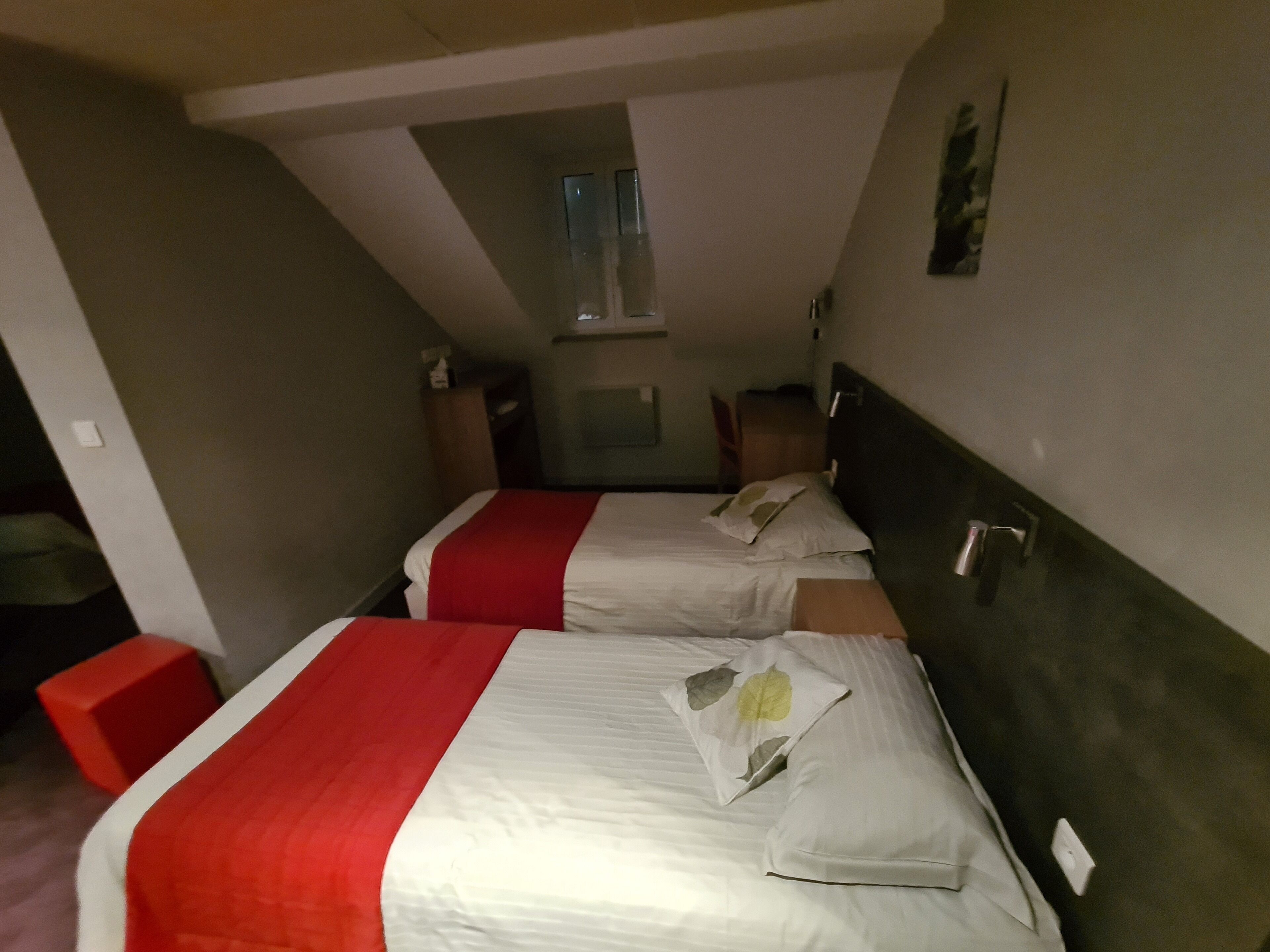 A hotel room with two beds, each with a red and white bedspread, and a small window above the beds.