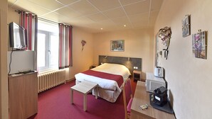 Habitación de hotel con cama, mesita de noche, escritorio, silla, radiador, cortinas, una obra de arte y televisor.