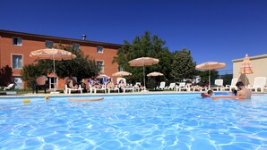 A swimming pool with lounge chairs and umbrellas, surrounded by a building with a tiled roof. - The Originals Boutique, Hôtel Le Pariou (Issoire)