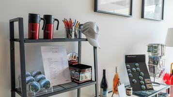 A metal shelf with red and black thermos flasks, a cap, and a jar of pencils. Below, there are tins of food and a wine bottle. A sign lists room rates, and a display of magnets is on the right.