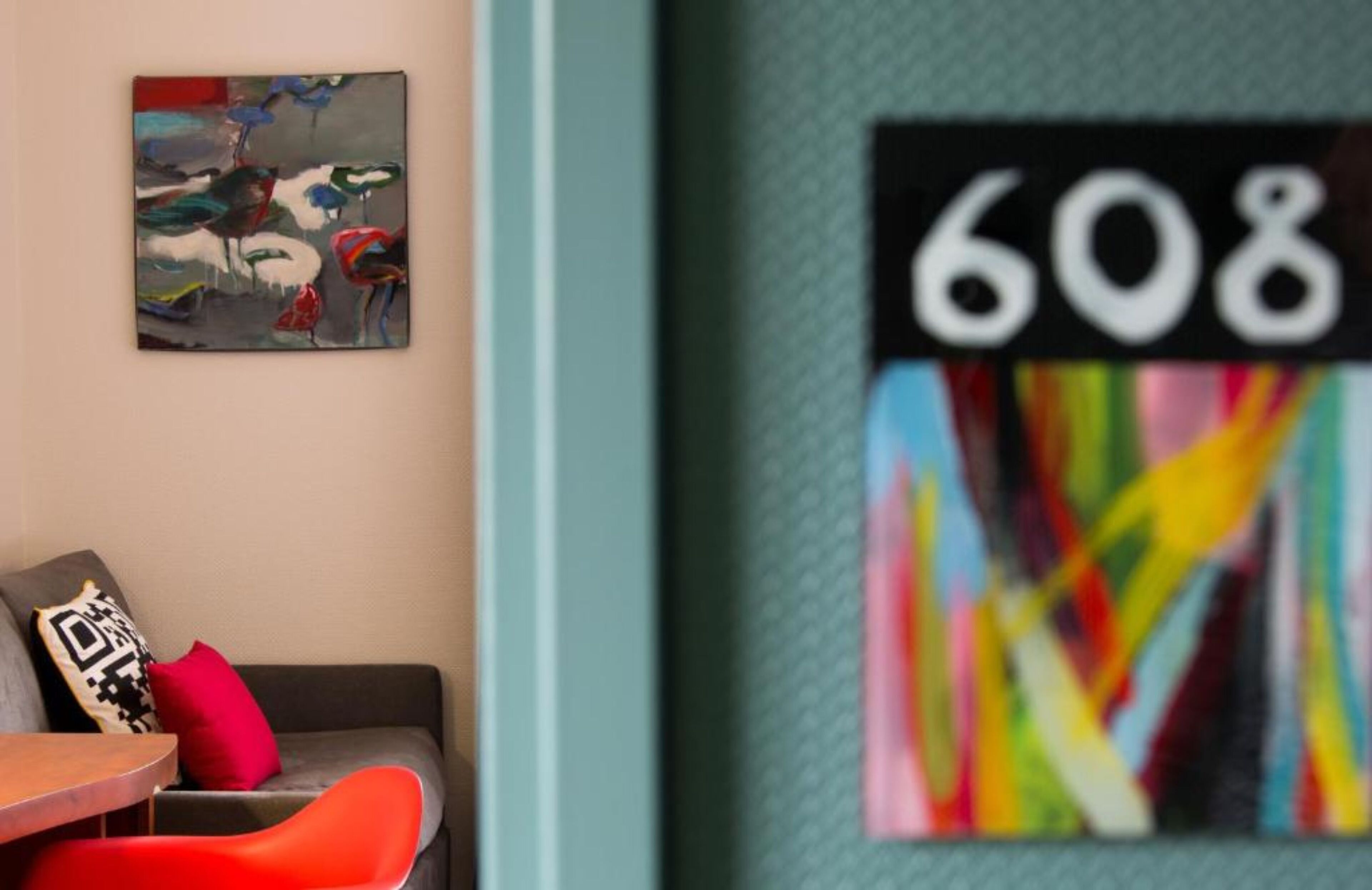 A room with a grey sofa, a red chair, a painting on the wall, and a colorful abstract artwork.