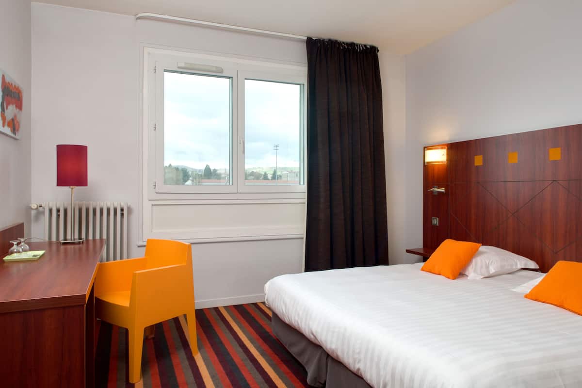 A hotel room with a bed, a desk, and a chair.