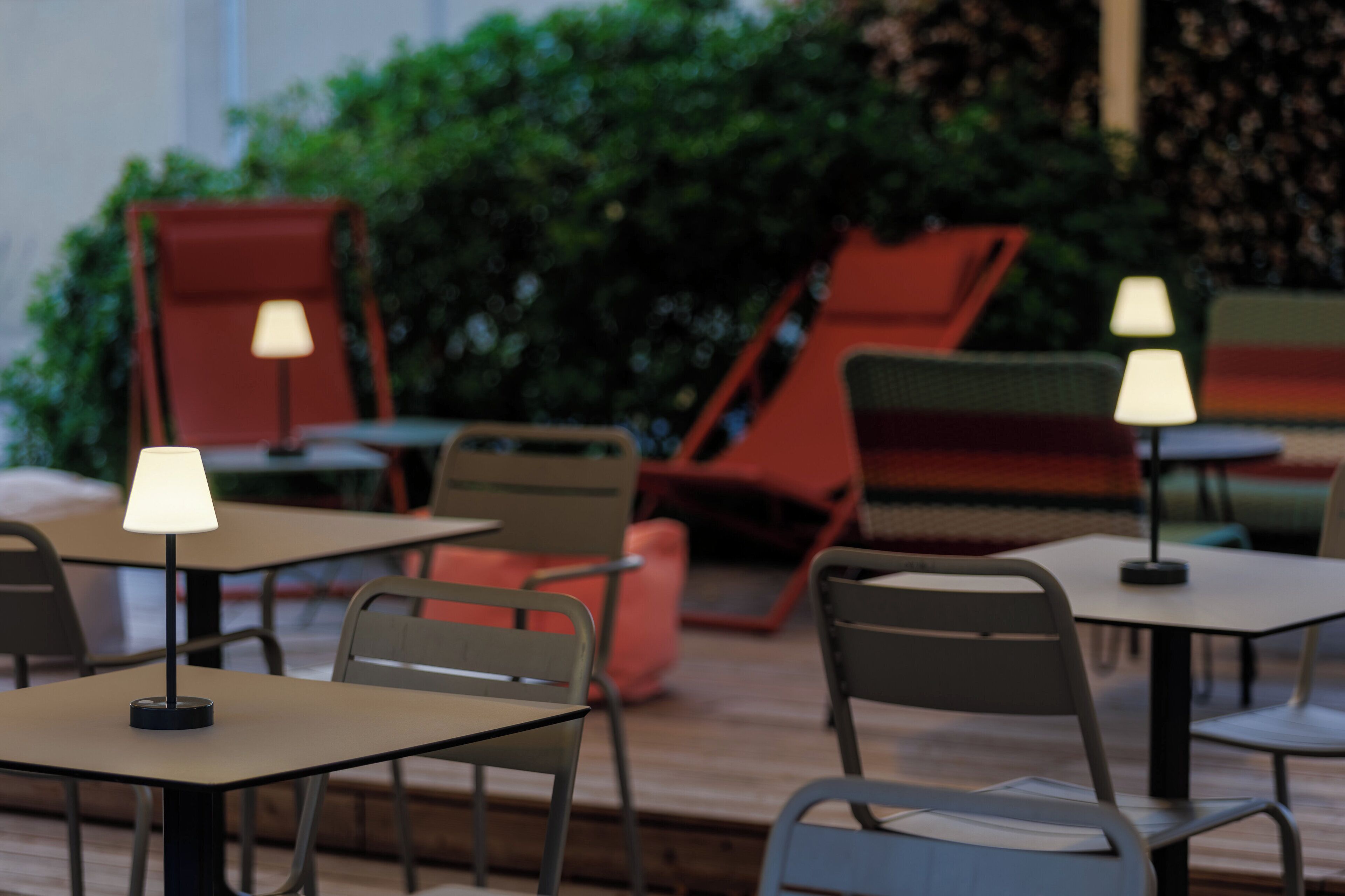 A modern indoor seating area with tables and chairs, some with lamps.