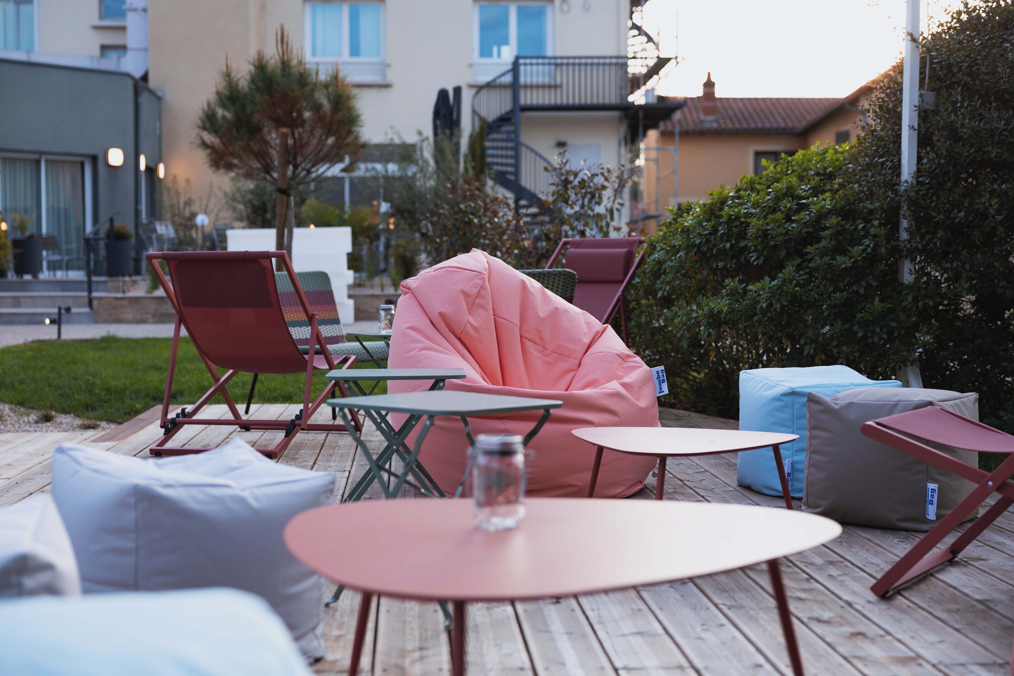 An outdoor patio with wooden tables and chairs, a pink bean bag, and a glass jar on one of the tables.