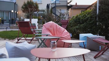 An outdoor patio with wooden tables and chairs, a pink bean bag, and a glass jar on one of the tables.