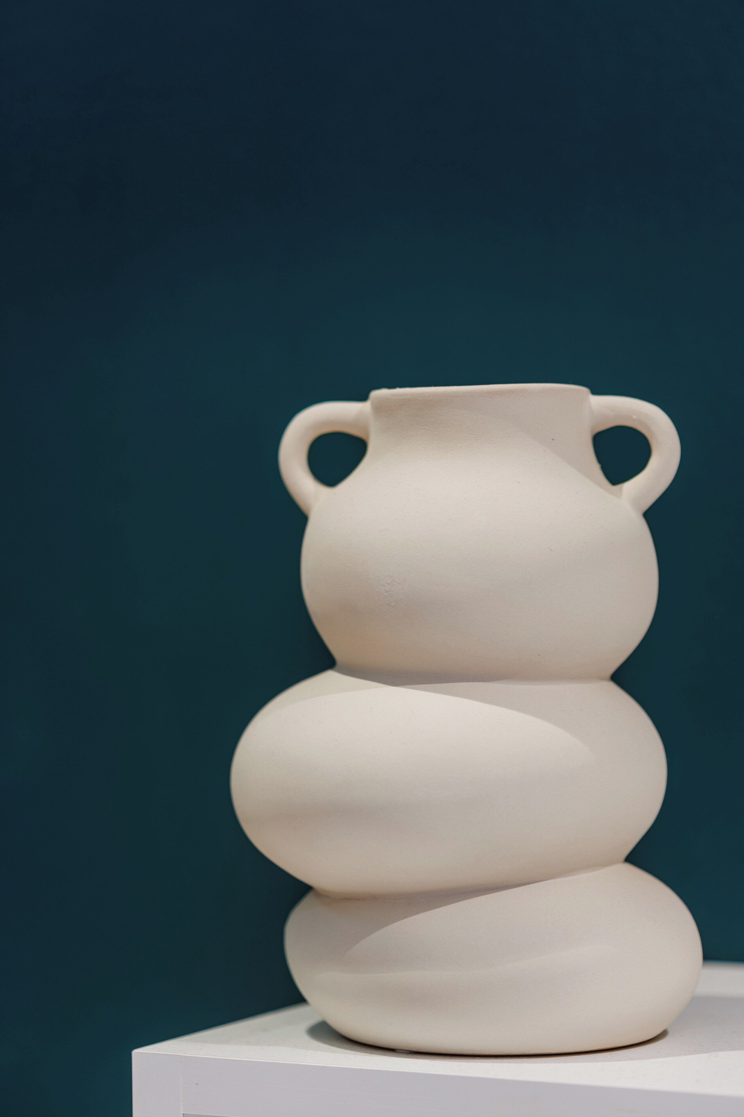 A white ceramic vase with two handles on a white pedestal against a dark background.