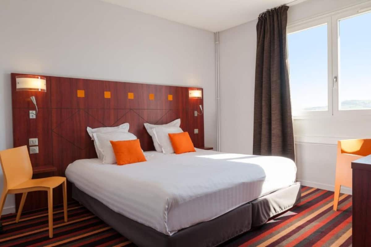 A hotel room with a large bed, two bedside tables, a chair, and a window with curtains.