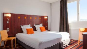 Una habitación de hotel con una cama grande, dos mesitas de noche, una silla y una ventana con cortinas.
