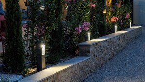 A landscaped garden with a stone wall, tall shrubs, and flowering plants. - The Originals Boutique, Hôtel Le Pariou (Issoire)