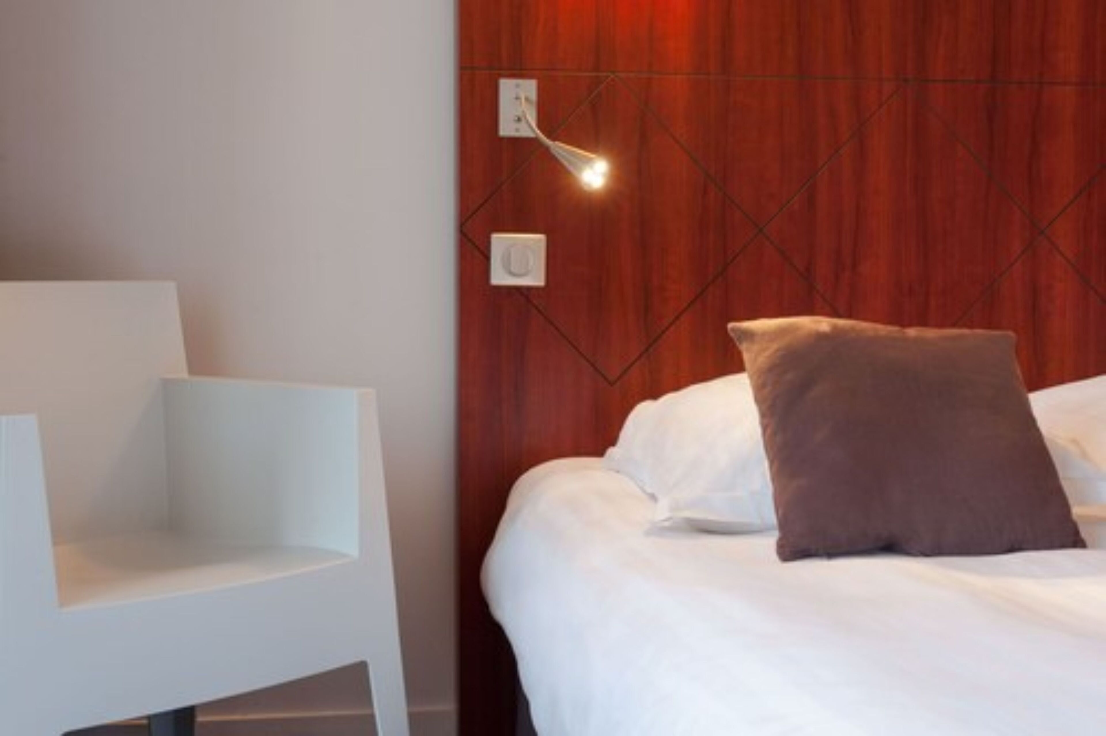 Een moderne hotelkamer met een houten hoofdeinde, een wit bed en een witte stoel.