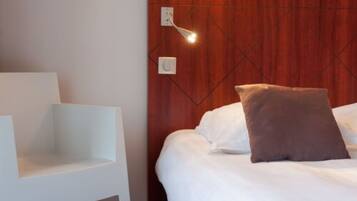 Een moderne hotelkamer met een houten hoofdeinde, een wit bed en een witte stoel.