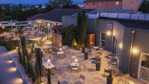 An outdoor patio area with multiple tables and chairs, surrounded by potted plants and umbrellas. - The Originals Boutique, Hôtel Le Pariou (Issoire)