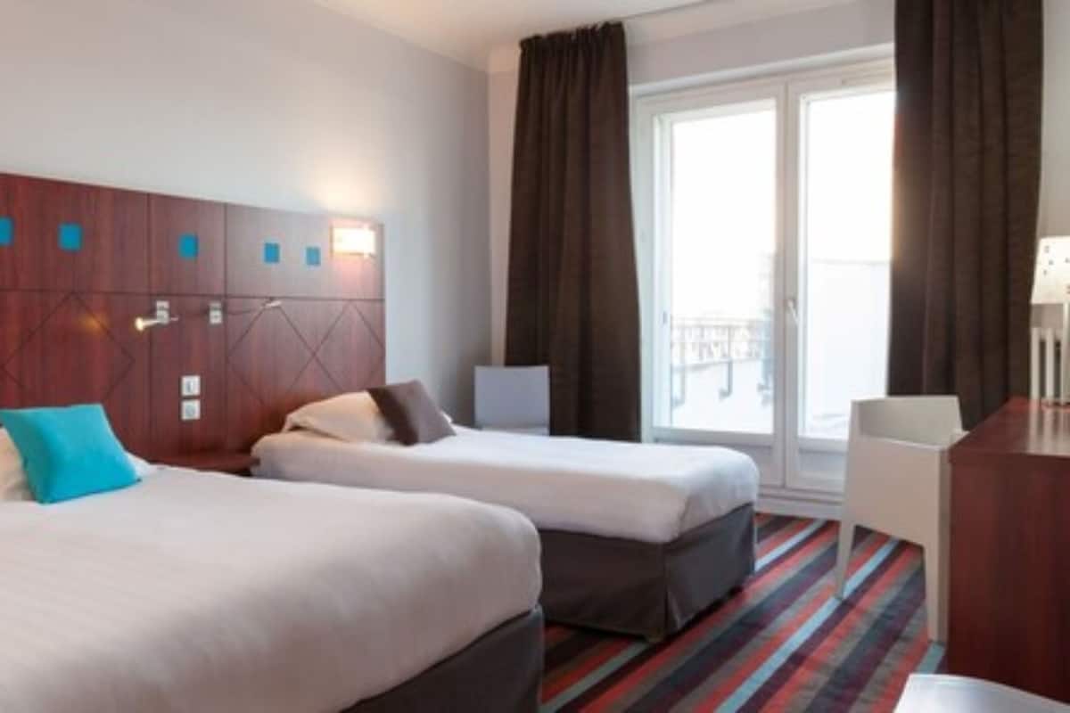 A hotel room with two beds, a wooden headboard, a window with curtains, and a striped carpet.